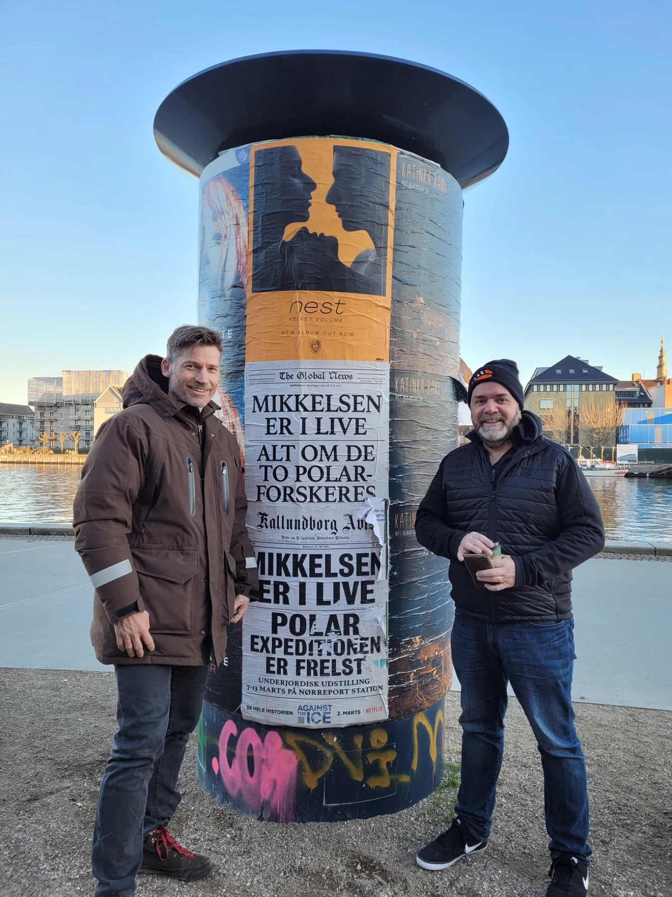 Nikolaj Coster-Waldau and Joe Derrick beside an Against the Ice teaser poster in Copenhagen